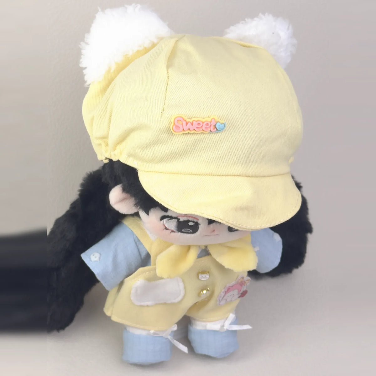 Cotton doll wearing the Sunny Kitten outfit: yellow overalls, light blue shirt, yellow neck bow, cat-ear cap and blue shoes, view from above